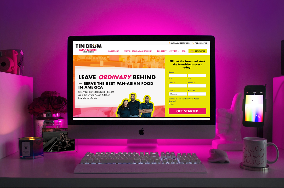 a desktop computer on a desk decorated with items, displaying the front of Tin Drum Asian Kitchen Franchise Design Development Website